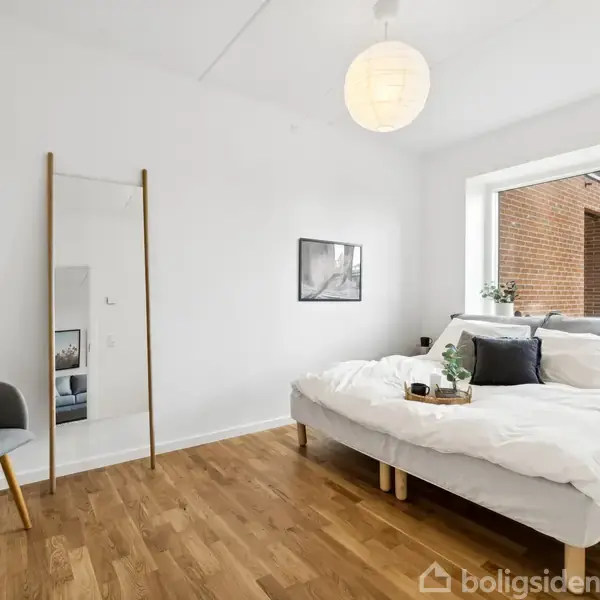 Badeværelse med en brusekabine adskilt af glasvæg, ophængt toilet, og hvidt skabsarrangement. Sorte og hvide håndklæder hænger på væggen, omgivet af hvide klinker og lofter.