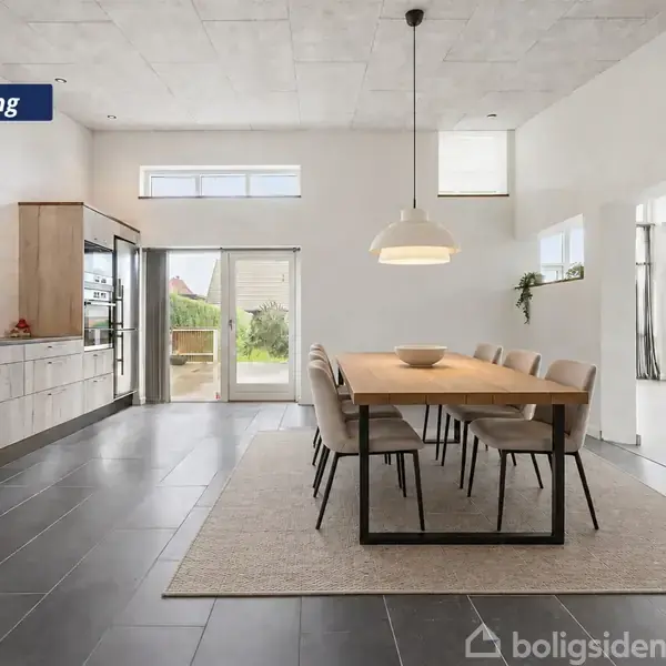 Spisestue med lang træbord og otte stole, står på et tæppe. Store glasdøre åbner mod en terrasse. Til venstre ses et moderne køkken. Tekst: "Visualisering".
