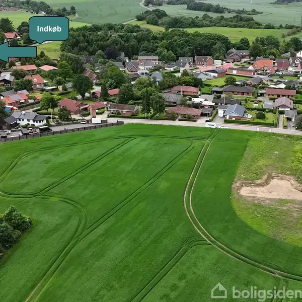 Luftfoto af et parcelhusområde med flere ledige byggegrunde afgrænset med røde linjer. Teksten "SOLGT" står flere steder på grunde, omgivet af grønne marker og et beboelsesområde.