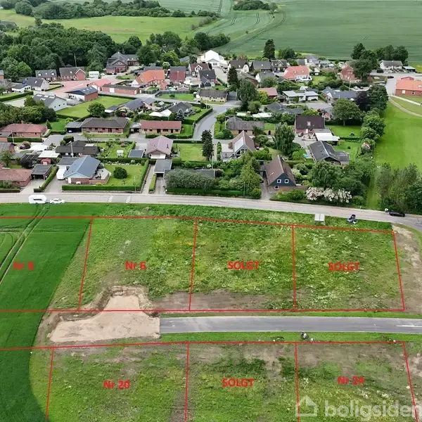 Grønne marker strækker sig mod en landsby med huse og træer. En tekstboks markør viser "Indkøb" over et område i landsbyen.