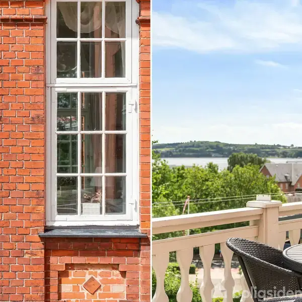 Røde mursten udgør en bygning med en hvidsprosset vindue. Ved siden af ses en terrasse med runde møbler og udsigt over en flod og grønne områder under en klar himmel.