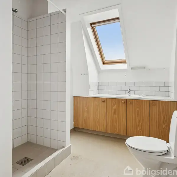 Et badeværelse med bruser, håndvask på træskab, og toilet. Rummet har et skråtag med et ovenlysvindue, der giver naturligt lys. Væggene er hvide, og bruseområdet har fliser.