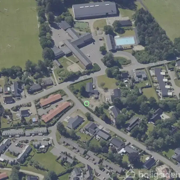 En bydel set oppefra med flere boligområder og veje omkranset af grønne områder. En sportsplads og en rektangulær swimmingpool er synlige blandt træerne.
