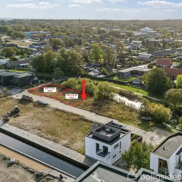 En tom byggegrund vist fra luften med to afmærkede byggefelter. En rød pil peger på felterne. Omkring grunden er der huse og træer i et boligområde. Tekst: "Grunde til salg 500 / 505 m2".