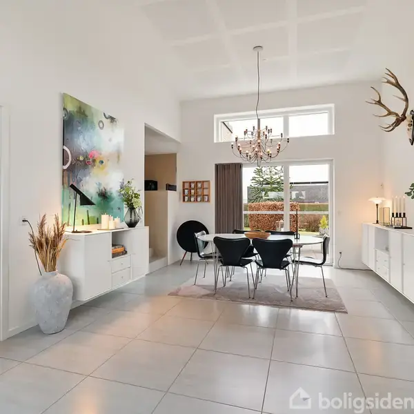 Spisestuemøbler står i et moderne rum med store gulvfliser. En lysekrone hænger over bordet, og en moderne kunstplakat er på væggen. Vinduer giver udsigt til en have.
