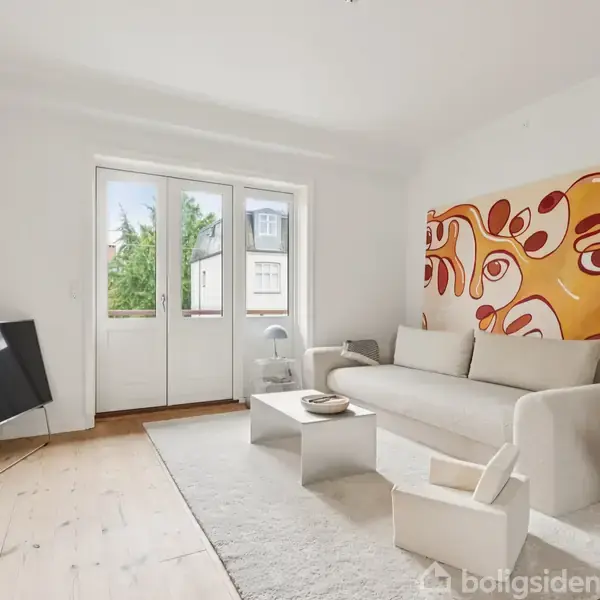 Hvid sofa står foran en væg med farverigt abstrakt maleri, fladskærms-tv til venstre. Rummet har lyse træbrædder og en glasdør, der åbner mod en udsigt med træer.