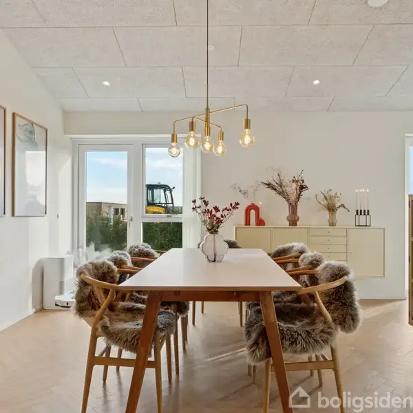 Moderne hus, terrassemiljø med to kurvestole og en grill. Rødstensvægge og store vinduer i baggrunden. Stilfuld fliseterrasse omsluttet af grøn græsplæne.