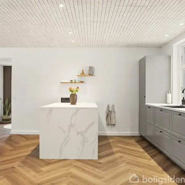 Køkkenø med marmoroverflade står i et rummeligt køkken med fiskebensparketgulv. Skabe og en vask er placeret under et stort vindue. Hylde med dekorationer er på væggen.