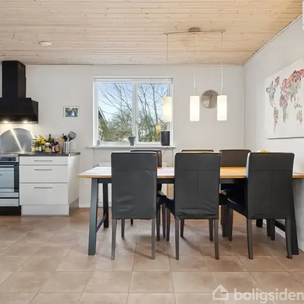 Sort læderhjørnesofa og lænestol står i en lys stue med trægulv, der har TV på væggen og vinduer mod terrassen med blomster på vindueskarmen.