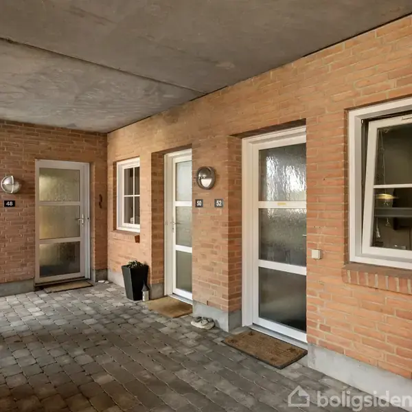 Tre døre side om side i en indre gårdsplads af mursten, hver med et vindue ved siden af. Dørmåtter foran dørene og en skraldespand ved den midterste dør.