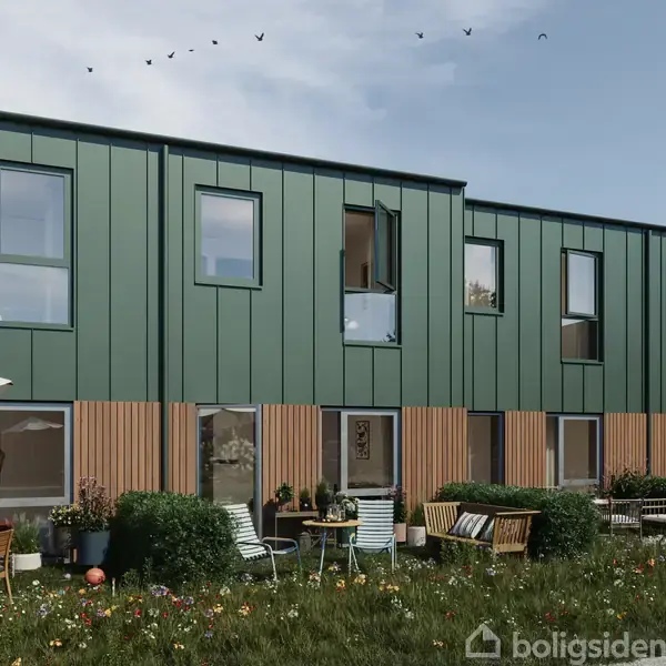 Rækkehuse med grøn facade og store vinduer, omgivet af en græsplæne med siddeområde og blomster, under en blå himmel med flyvende fugle.