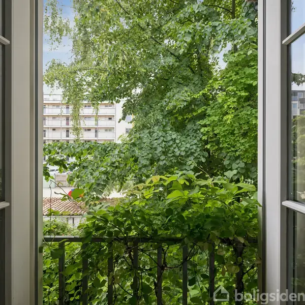 Åbne altandøre, der fører ud til en lille balkon med udsigt til tætte grønne træer. I baggrunden ses en bygning med hvide facader. Ingen tekst til stede.
