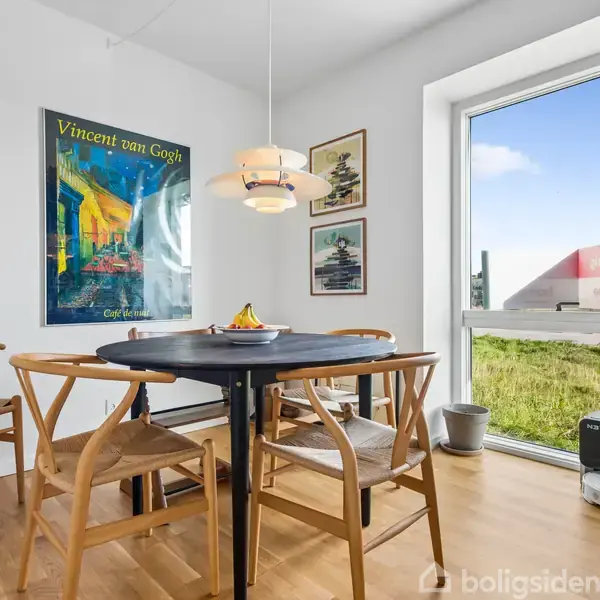 Et rundt bord omgivet af fire træstole står i et lyst rum. På væggen hænger en Vincent van Gogh-plakat og to billeder. En stor vindue giver udsigt til græsplæne.