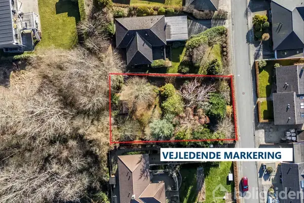 Bygning og have set oppefra, omkranset af træer og buske; en vej løber langs højre side. Tekst: "VEJLEDENDE MARKERING".