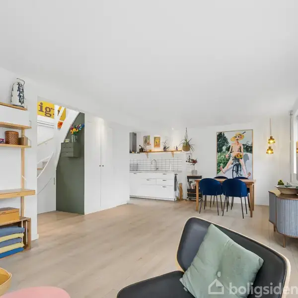Stue med moderne indretning; en grå stol står i forgrunden. I baggrunden ses et spisebord med blå stole og en enkeltsidet køkkenhylde. Plakaten på væggen viser en person.