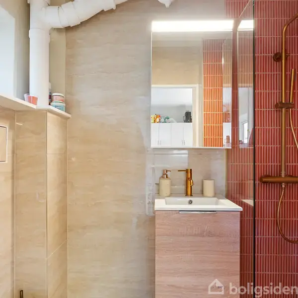 Et badeværelse med en håndvask og et spejlskab over. Brusekabinen er til højre med røde fliser og en regnbruser. Vinduet sidder til venstre, delvist synligt.