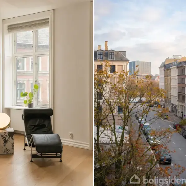 Lænestol står ved et vindue med udsigt til gaden, mens en lampe og en plante står på et bord. Udenfor ses en byvej omgivet af træer og bygninger.