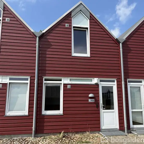 Rødt rækkehus med hvid dør og vinduer, beliggende i et boligkvarter. Husnummeret "110" er ved siden af døren. Himmel med få skyer i baggrunden.