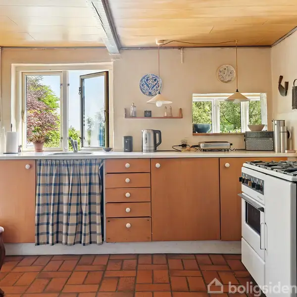 Et køkken med træskabe og en åben dør til haven. En gaskomfur til højre, flisegulv og keramikdekorationer skaber en hyggelig atmosfære. Stribet gardin skjuler skab.