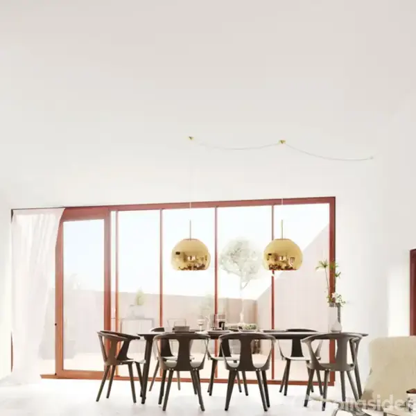 Spisebord med otte stole står under to gyldne lamper. Store vinduer i baggrunden giver lysindfald. Rummet er lyst og moderne med hvidmalede vægge og minimalistisk indretning.