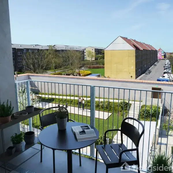 En altan med et cafébord og to stole står stille, omgivet af potteplanter. Udsigten viser en boligbygning og grønne områder i et bymiljø.