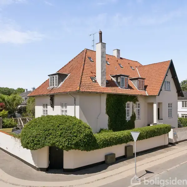 Stor hvid villa med rødt tegltag står på en hjørnegrund i et roligt villakvarter. Omkranset af lave hække, med en parkeret bil på vejen foran huset.