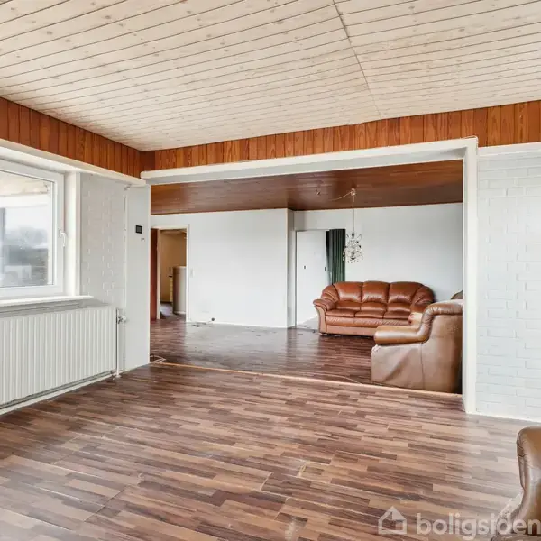 Gult murstenshus står stille i et snedækket landskab ved siden af en vej. Huset har gavltag og en glasveranda. Træer og en gadelampe omkranser scenen.
