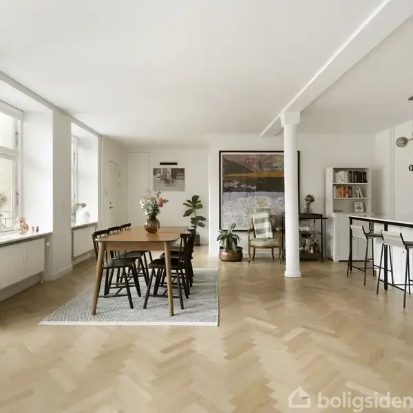 En moderne stue med lyse trægulve, hvor et spisebord med seks stole står midt på et tæppe. Til venstre er der store vinduer, og til højre en bar med høje stole. En plante og et maleri er i baggrunden.