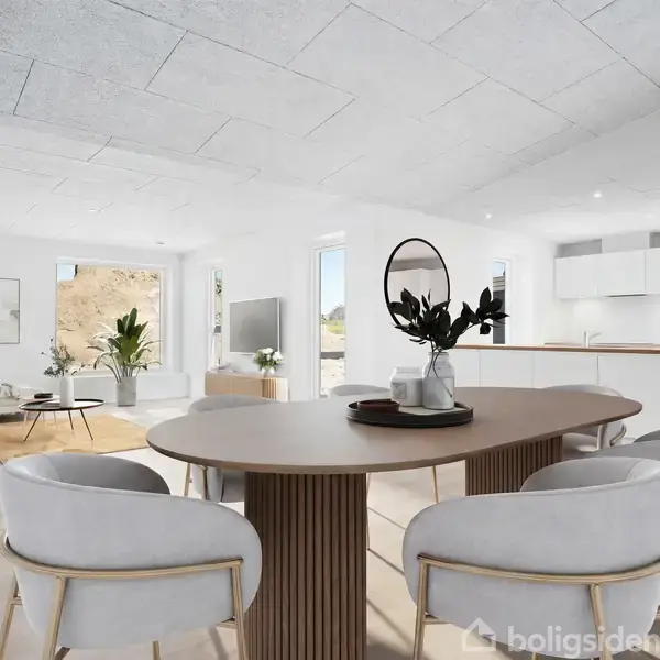 Et ovalt spisebord med dekoration står i et moderne, lyst køkkenalrum med hvide vægge. Der er elegante stole omkring bordet og et stilfuldt åbent køkken i baggrunden.