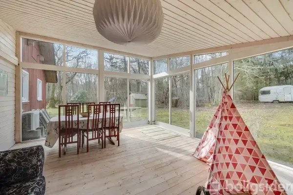 En entré med en dør med glasparti, en bænk med sko under og en knagerække. Teksten "Carpe Diem" ses over en døråbning til et køkken med træloft.