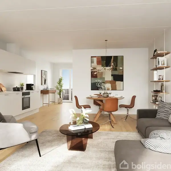 Stue med grå sofa og lænestol placeret omkring et rundt sofabord. Til højre hænger kunst på væggen. Køkkenet med hvide skabe og spisebord ses i baggrunden.