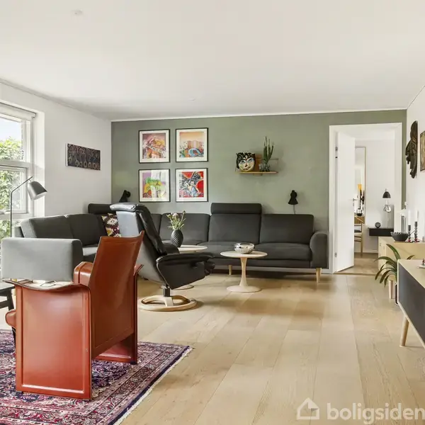 Stue med sofa- og lænestuearrangement, hvor handlingspunktet er stilfulde møbler. Kontekst er et lyst rum med en grøn væg, kunstbilleder, vinduer og et rødt tæppe på trægulvet.