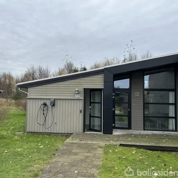 Et moderne, fladt taghus står på en plet af græs. En stenlagt gangsti fører til en glasdør på siden af huset. En ledning hænger på muren.