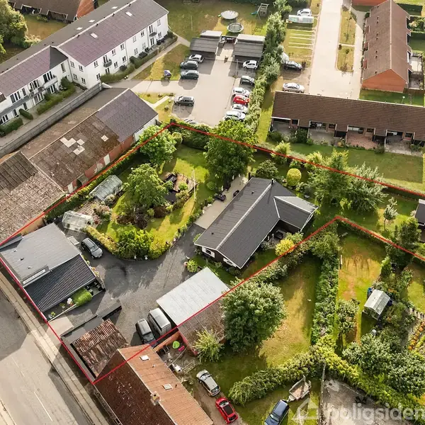 Hus set fra oven, omkranset af en rød streg. Det har en have med træer og en lille bygning. Omgivet af andre huse og vej i et boligområde.