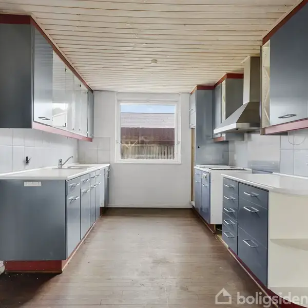Et rummeligt køkken med blå skabe, hvid bordplade og træloft. Vindue for enden giver dagslys. Rummets åbne layout giver en funktionel arbejdsplads.