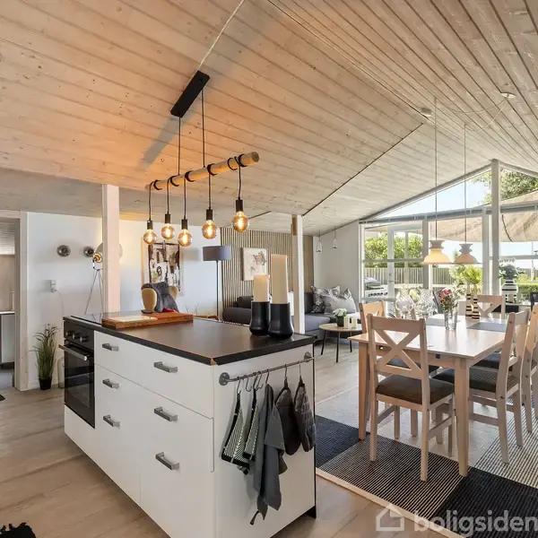 Sort lænestol med fodskammel står i et lille, lyst rum med loft af træplanker. Ved siden af står et lille bord med en plante. Væggene har malerier og en hylde.