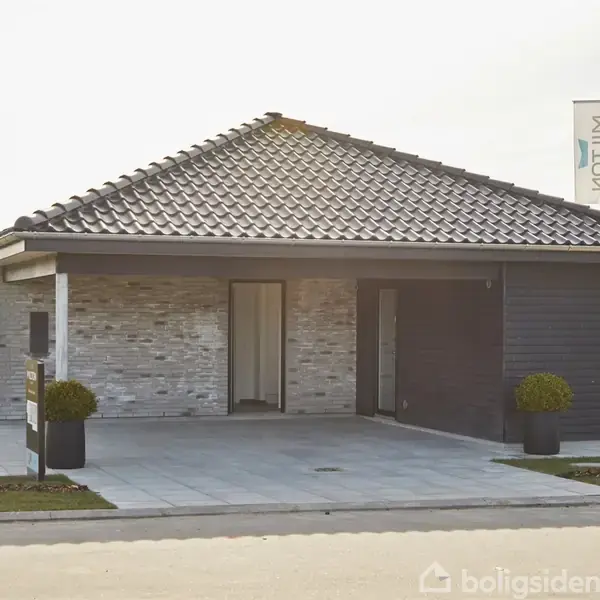 En moderne bungalow med fladt tegltag står stille i et solrigt kvarter. Huset er lavet af lyse mursten med sorte detaljer. To krukker med små planter flankerer indgangspartiet.