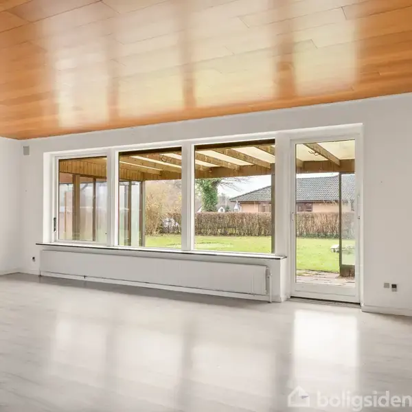 Stort, tomt værelse med lyse vægge og trægulv. Store vinduer og en glasdør åbner ud til en overdækket terrasse og en grøn have. Træloft skaber varme.