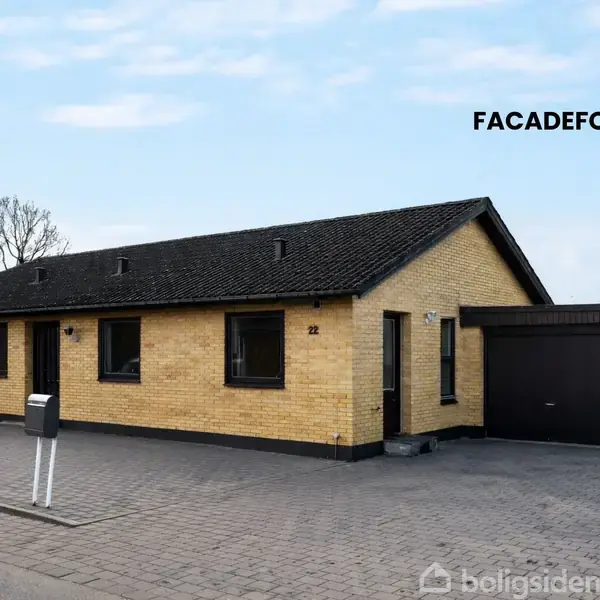 Et gult murstenshus med sort tag står på en flisebelagt grund. Til højre ses en garage med sort port. Tekst i billedet: "FACAEFORSALG". En postkasse er placeret foran huset.