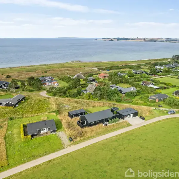 Huse ligger spredt i et grønt landskab med havudsigt i baggrunden. Området er kuperet med veje, træer og græs. Det er et kystnært boligområde.