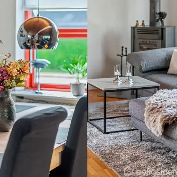 Vase med blomster på spisebordet under moderne lamper. Gråt sofaarrangement med tæppe og sofabord, placeret ved brændeovn i hyggelig stue med lyse vægge.
