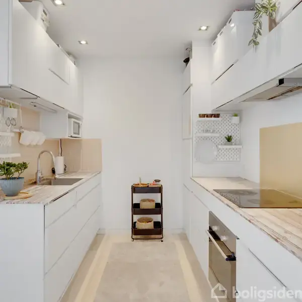 Et moderne køkken med hvide skabe og en indbygget ovn. Der er en kogeplade på bordpladen. Små planter pynter rummet, som er lyst og minimalistisk indrettet.