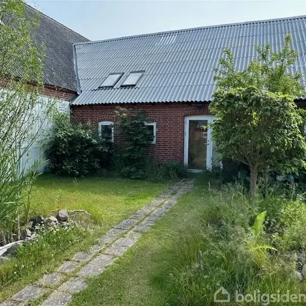 Et rødt murstenshus med tagvinduer, omgivet af en frodig have med græs, buske og træer. En smal stensti fører op til en hvid hoveddør.