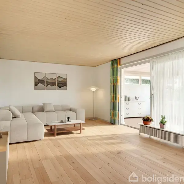 Sofa står i stuehjørnet, flankeret af en gulvlampe og et lille sofabord. Rummet er lyst med trægulve, hvide vægge og store vinduer med farverige gardiner.