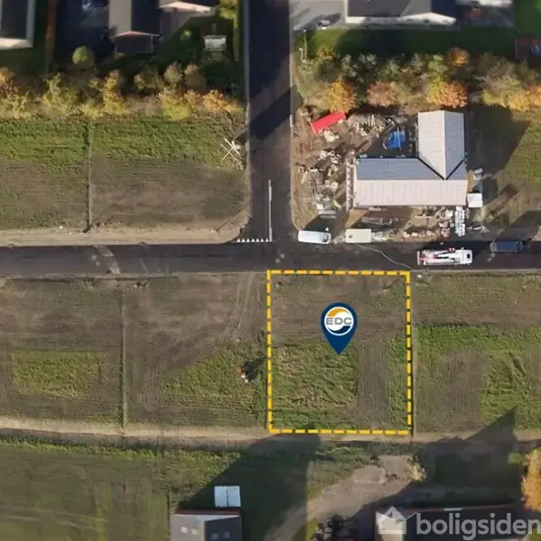 Tomt markeret af EDC ligger i et grønt område omgivet af vejnet og bebyggelse. Omkringliggende træer og en bygning ses nordligt.