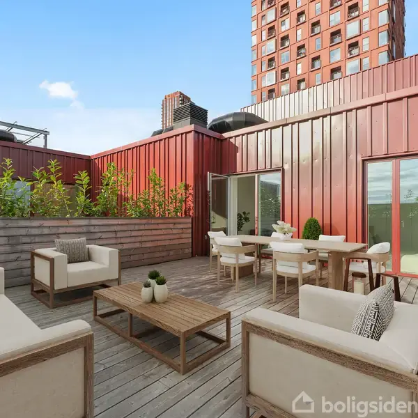 Terrasse med hvide møbler placeret omkring et lavt træbord. Solbeskinnet med udsigt til rødbrune bygningers facader og grønne planter langs kanterne. Moderne bymiljø i baggrunden.