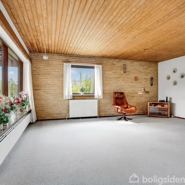 Et stort rum med en læderstol står foran en murstensvæg. Rummet har et stort vindue med udsigt til en have og potteplanter på vindueskarmen. Vægge pyntet med tallerkener.