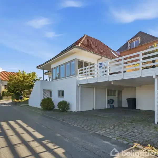 Hvidt hus med rødt tag står i en grøn have. En kort trappe fører op til hovedindgangen på husets front. Omkringliggende træer og nabohuse udgør det naturskønne kvarter.