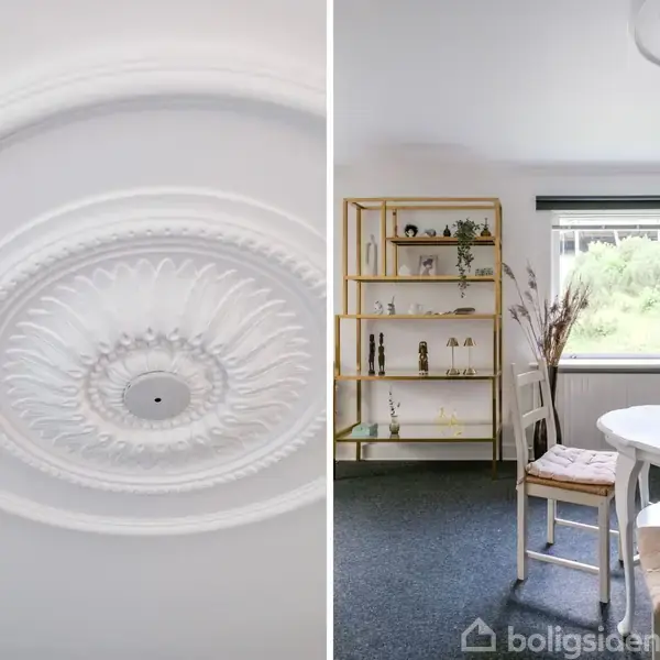 Loftroset i detaljeret hvidt design hænger i loftrum. Ved siden af er et lyst rum med rundt spisebord, stole, hylde med dekorationer og vindue med udsigt til grønne omgivelser.