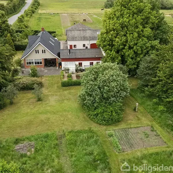En stor bygning omringet af frodige træer og en velplejet have. Ved siden af bygningen er en vej der strækker sig gennem det grønne landskab.